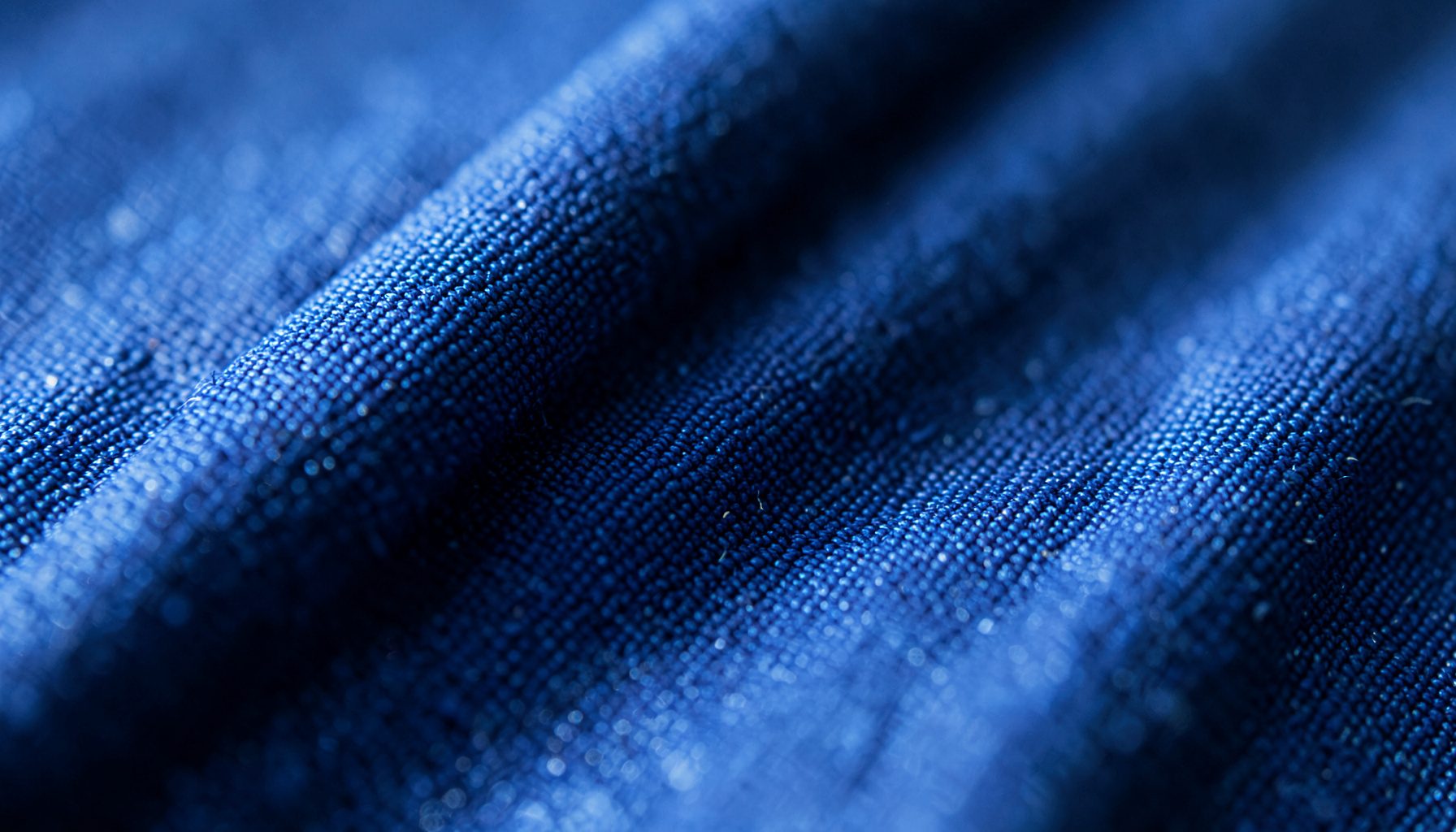 Extreme close-up photograph of fine indigo and steel-blue fabric weave, with soft diagonal light catching the threads, conveying warmth and quiet resilience.